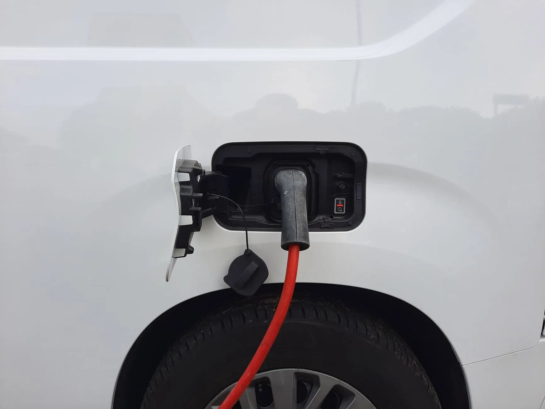 A white electric van charging, a red cable plugged into its side inlet