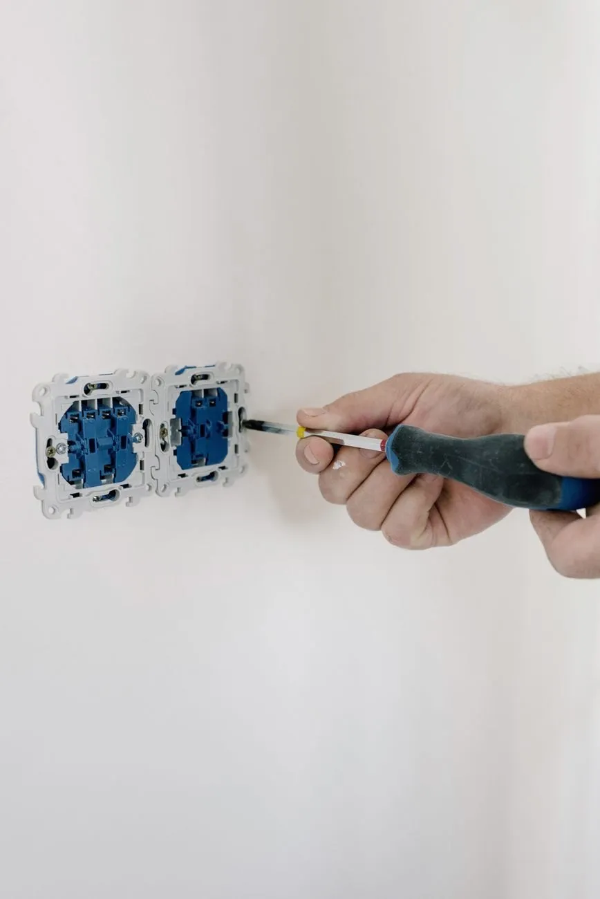 A hand tightening a socket module with a screwdriver on a white wall